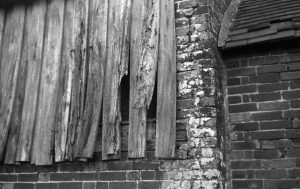 Black and white photograph taken with voigtlander vito 1 film camera of a close up detail of brick and weathered old wood shiplap